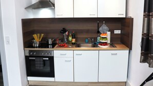 Une cuisine compacte avec des meubles blancs, une hotte en acier inoxydable et un four encastré.