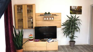 Un salon avec un meuble en bois, un téléviseur à écran plat, une plante en pot et un tableau accroché au mur.