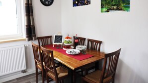 Un coin repas avec une table en bois, des chaises, une horloge et deux tableaux encadrés accrochés au mur.