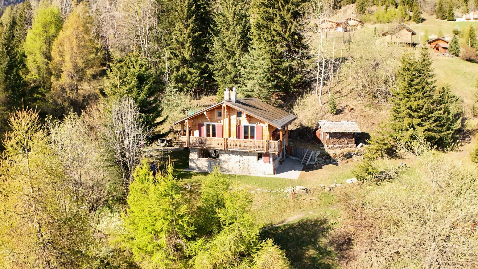 A wooden cabin with a balcony, surrounded by dense forest and a stone foundation.