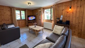 A cozy living room with a flat-screen TV, wooden walls, a sofa, a coffee table, and a radiator.