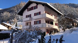 A multi-story building with balconies, surrounded by snow-covered trees and a mountainous backdrop.