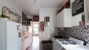 A compact kitchen with white cabinets, a gas stove, and a small trash bin.