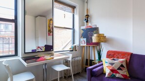 A modern room with a desk, white chairs, a purple sofa, and a large window.