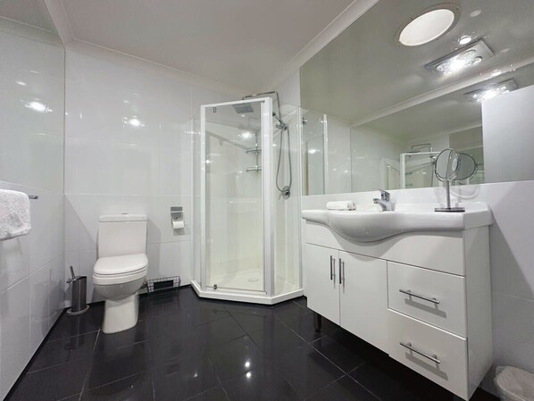 A modern bathroom with a toilet, a glass-enclosed shower, and a vanity with a mirror.
