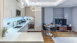 Eine moderne Küche mit Einbauofen, einem Essbereich mit rundem Tisch und Stühlen sowie einem an der Wand montierten Flachbildfernseher.