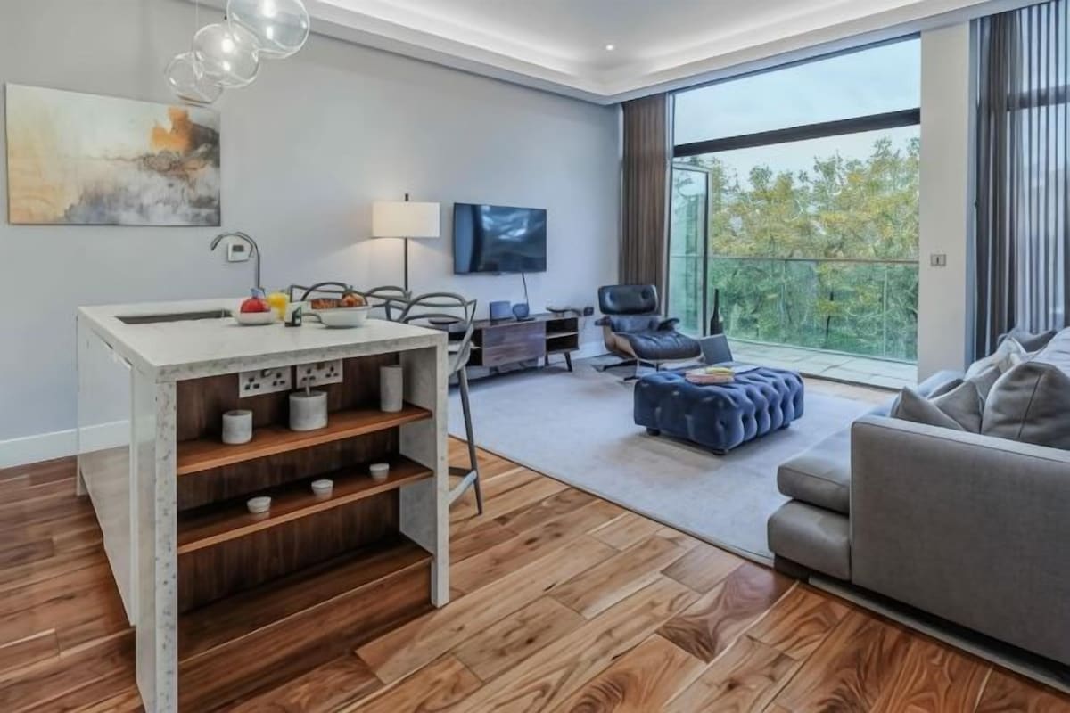 A modern living room with a sofa, a dining area with a table and chairs, a TV mounted on the wall, and a balcony with a view.