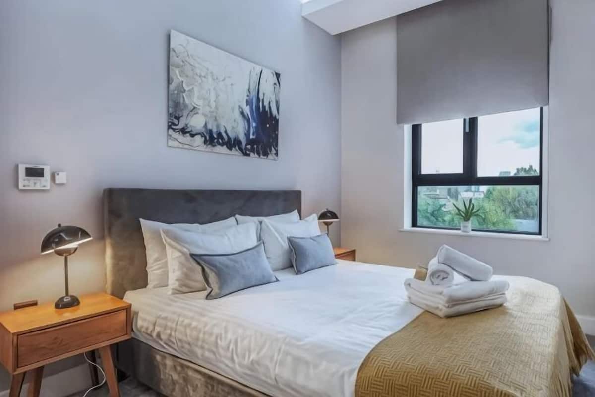 A bedroom with a bed, bedside tables, a window, and a painting on the wall.
