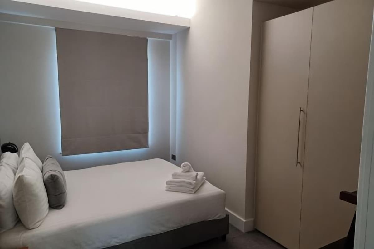 A bedroom with a bed, pillows, a window, and a wardrobe.