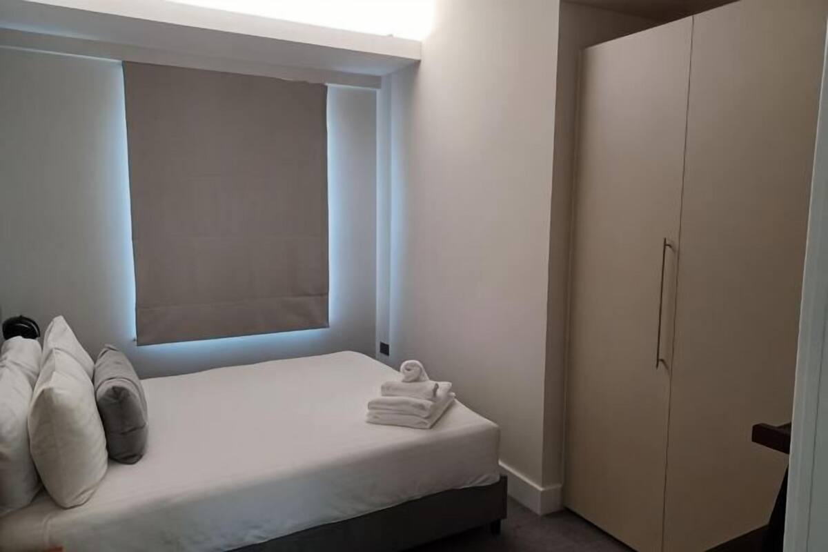 A bedroom with a bed, pillows, a window, and a wardrobe.