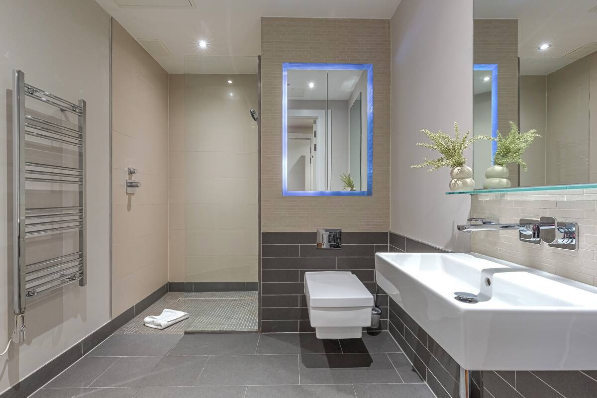 A modern bathroom with a glass shower enclosure, a white sink, and a large mirror.