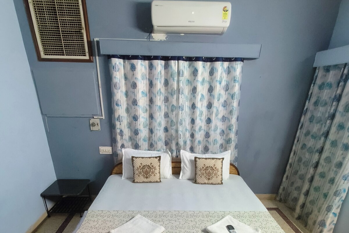 Een slaapkamer met een bed, een airconditioningapparaat, gordijnen en een kamerbreed tapijt met patroon.