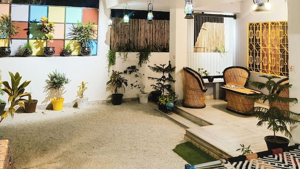 A hostel with a sign reading "OHH HOSTLER," outdoor seating with chairs and tables, and potted plants around.