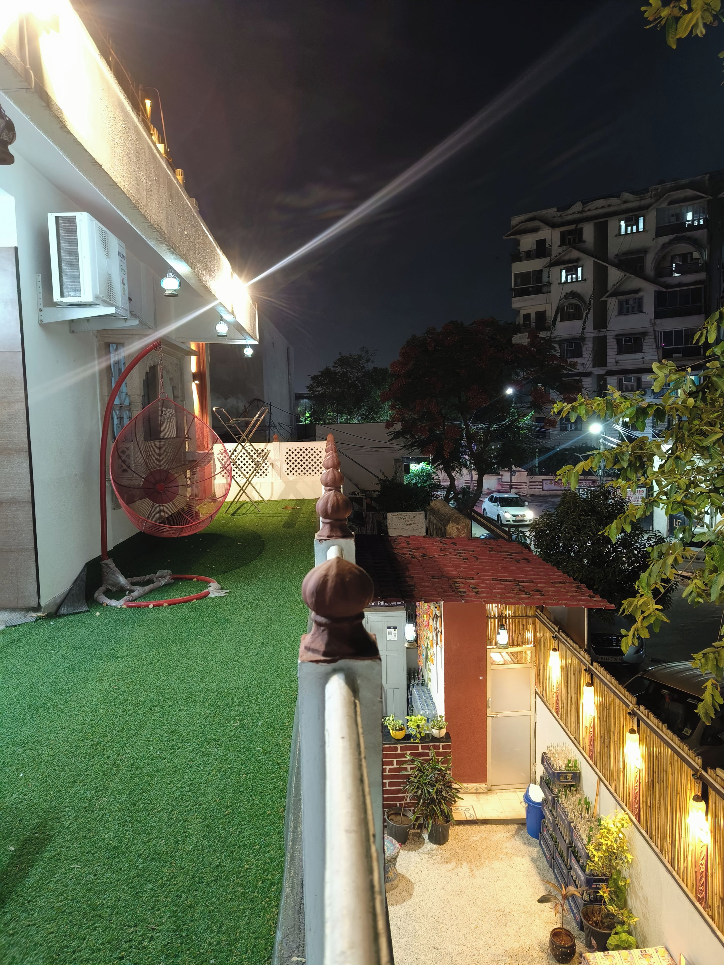 A balcony with a view of a building, artificial green turf, and a red hanging chair.