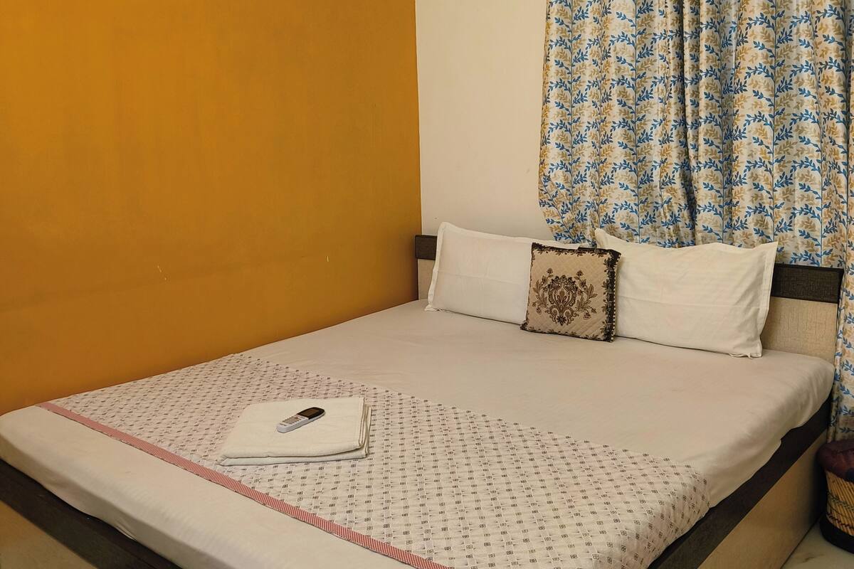 Un lit bien fait, avec une couvre-lit à motifs, un oreiller et une télécommande posée dessus.