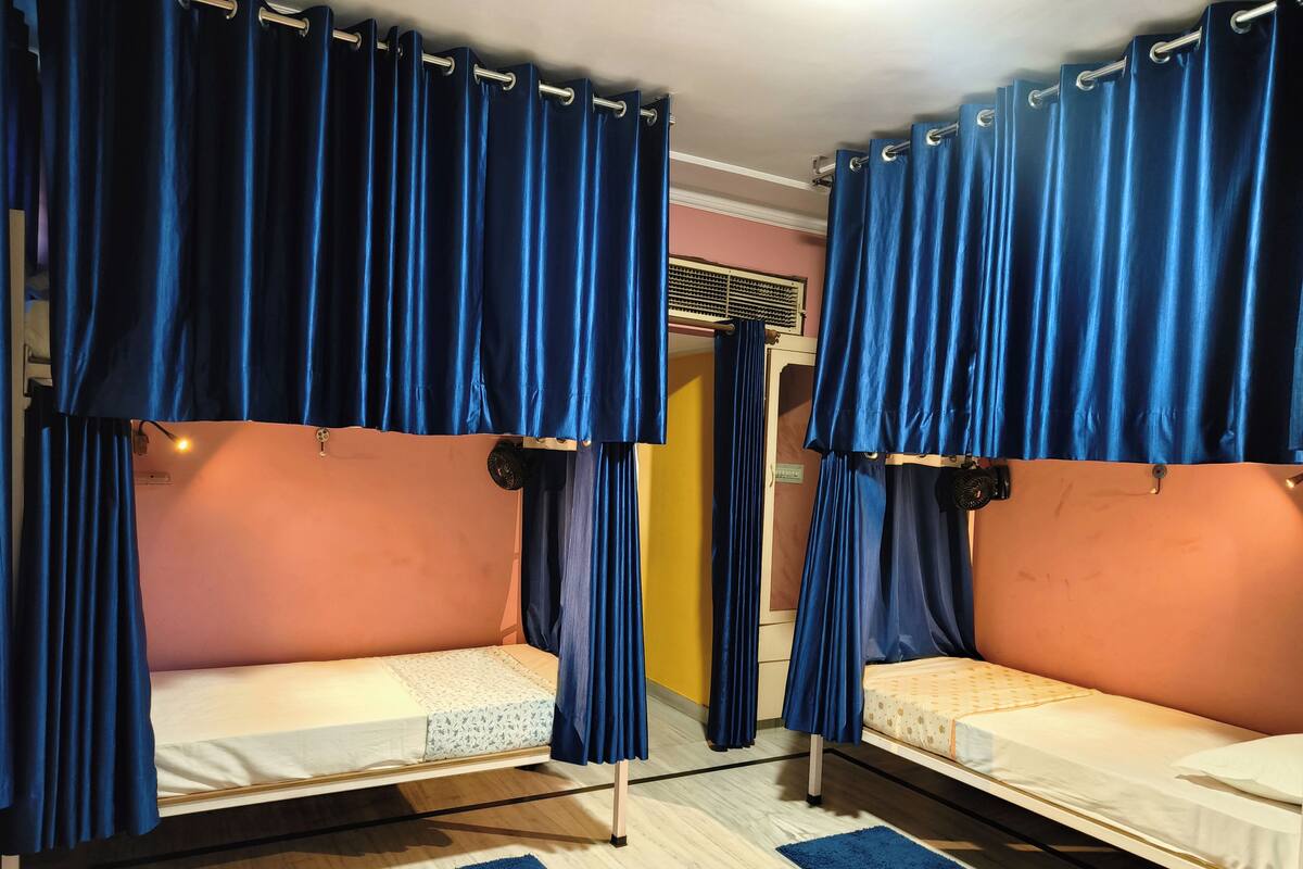 Une chambre avec deux lits superposés, chacun étant muni d’un rideau bleu. Il y a un petit tapis sur le sol et une paire de chaussures à côté du lit.