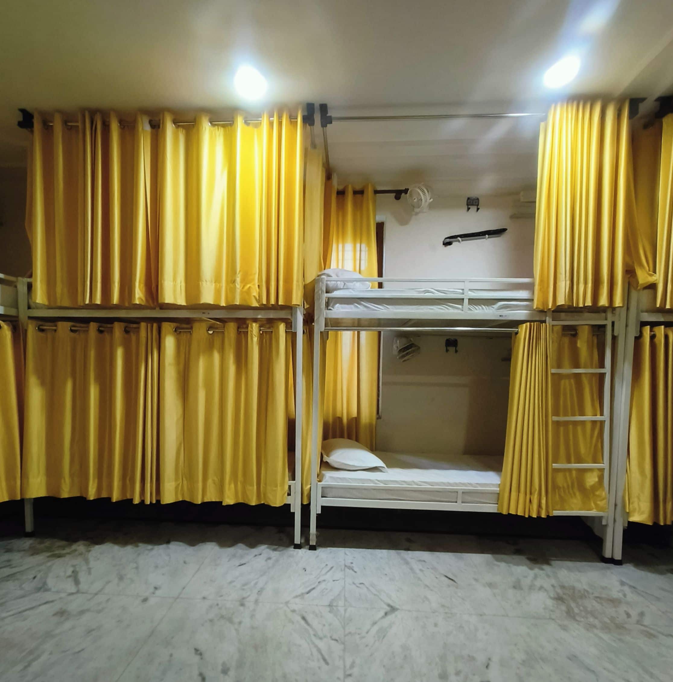 A bunk bed room with yellow curtains, a fan, and a ladder.