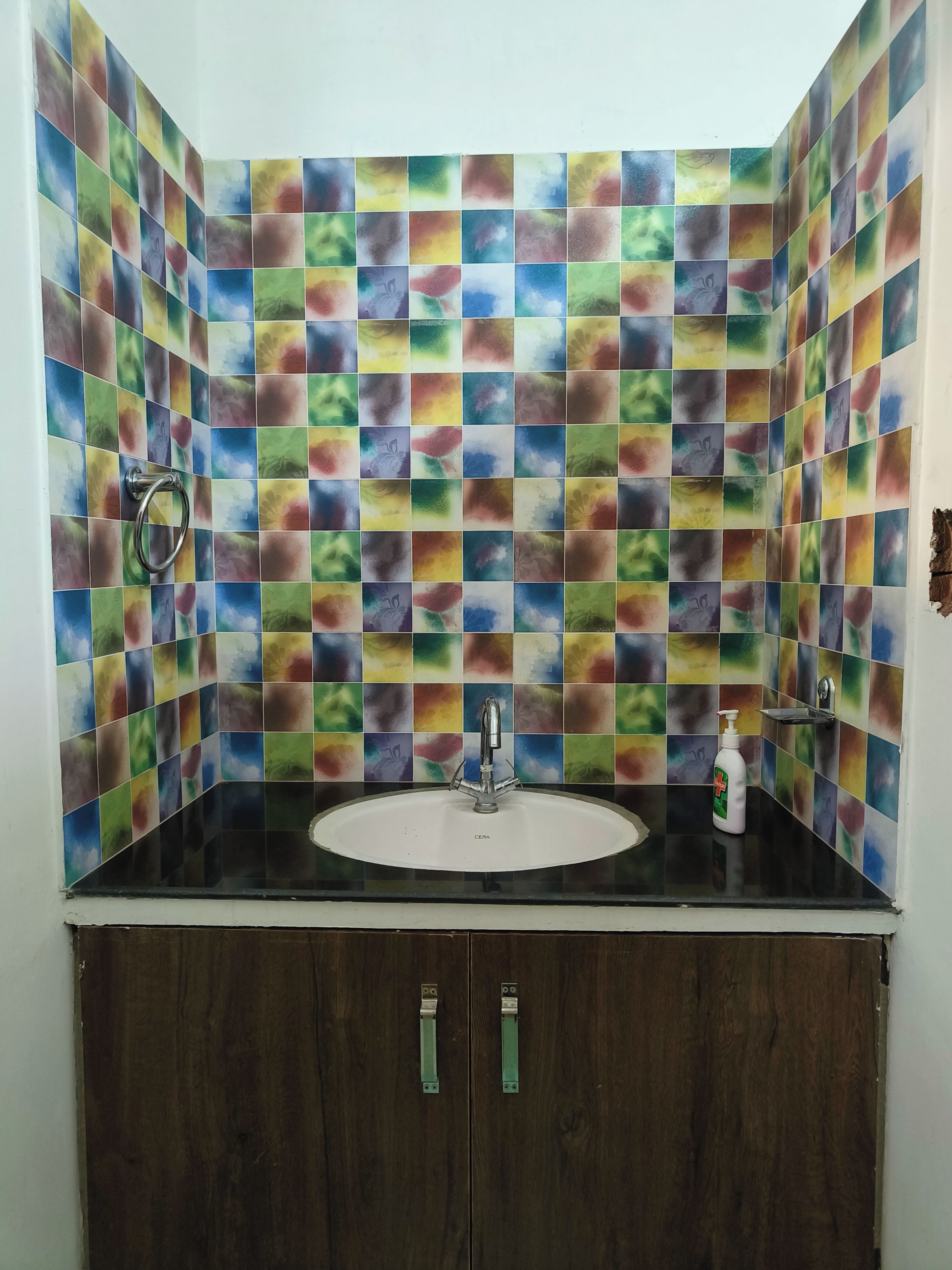 A bathroom with a colorful mosaic tile backsplash, a white sink, and a dark wooden cabinet.