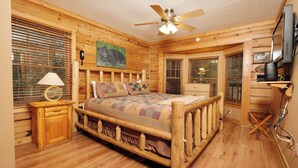 A wooden cabin bedroom with a bed, a nightstand, a lamp, a ceiling fan, and a television. - 2BR GBurg log cabin- hot tub, dog friendly! (Gatlinburg)