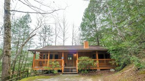 A cabin with a wooden porch, a chimney, and a dirt driveway surrounded by trees. - 2BR GBurg log cabin- hot tub, dog friendly! (Gatlinburg)