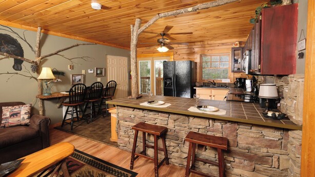 A rustic cabin interior with a stone bar, wooden furniture, and a ceiling fan. - 2BR GBurg log cabin- hot tub, dog friendly! (Gatlinburg)