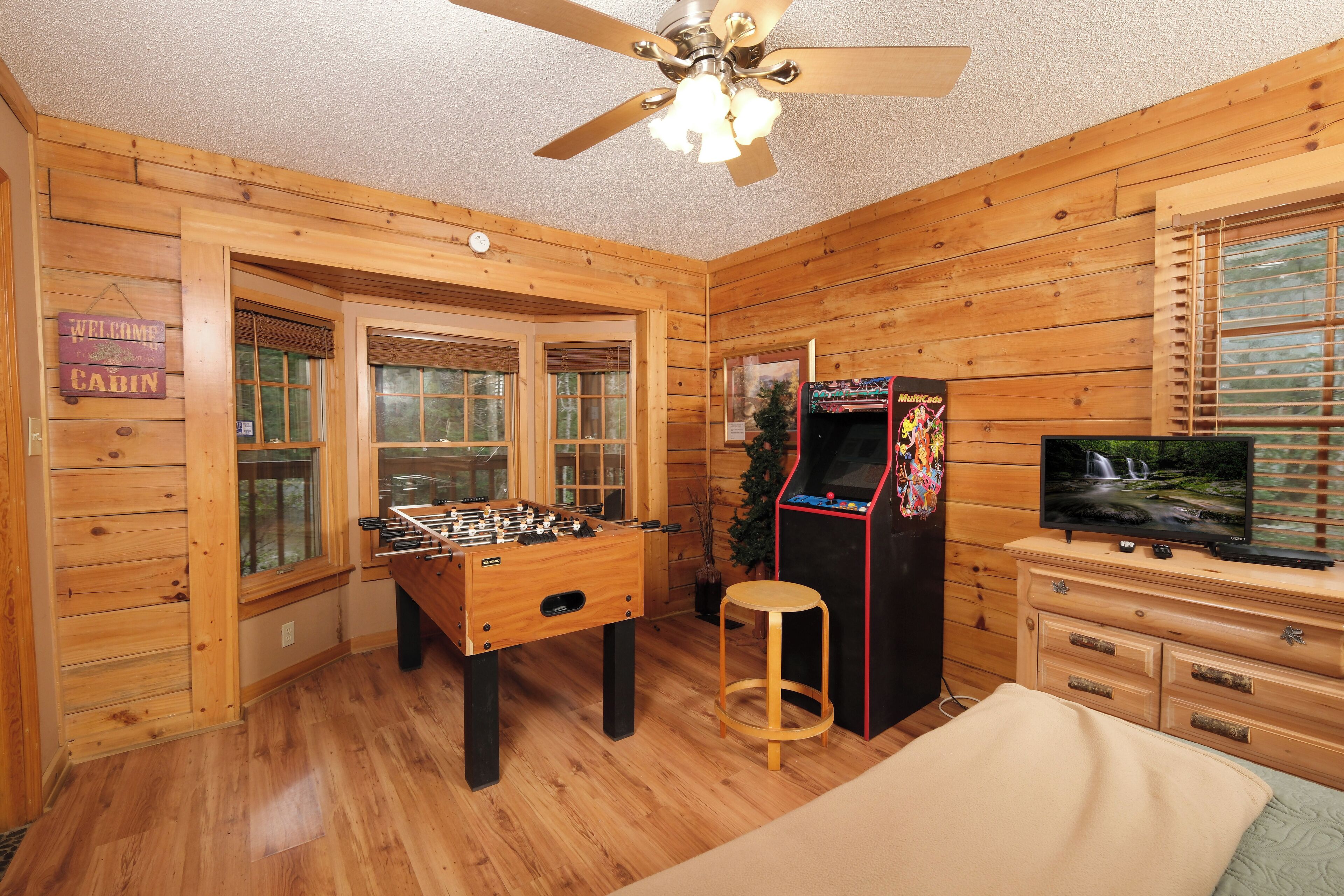 A wooden cabin interior with a foosball table, a television, and a ceiling fan.