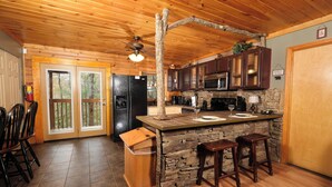 A rustic kitchen with wooden cabinets, a stone island, and a ceiling fan. - 2BR GBurg log cabin- hot tub, dog friendly! (Gatlinburg)