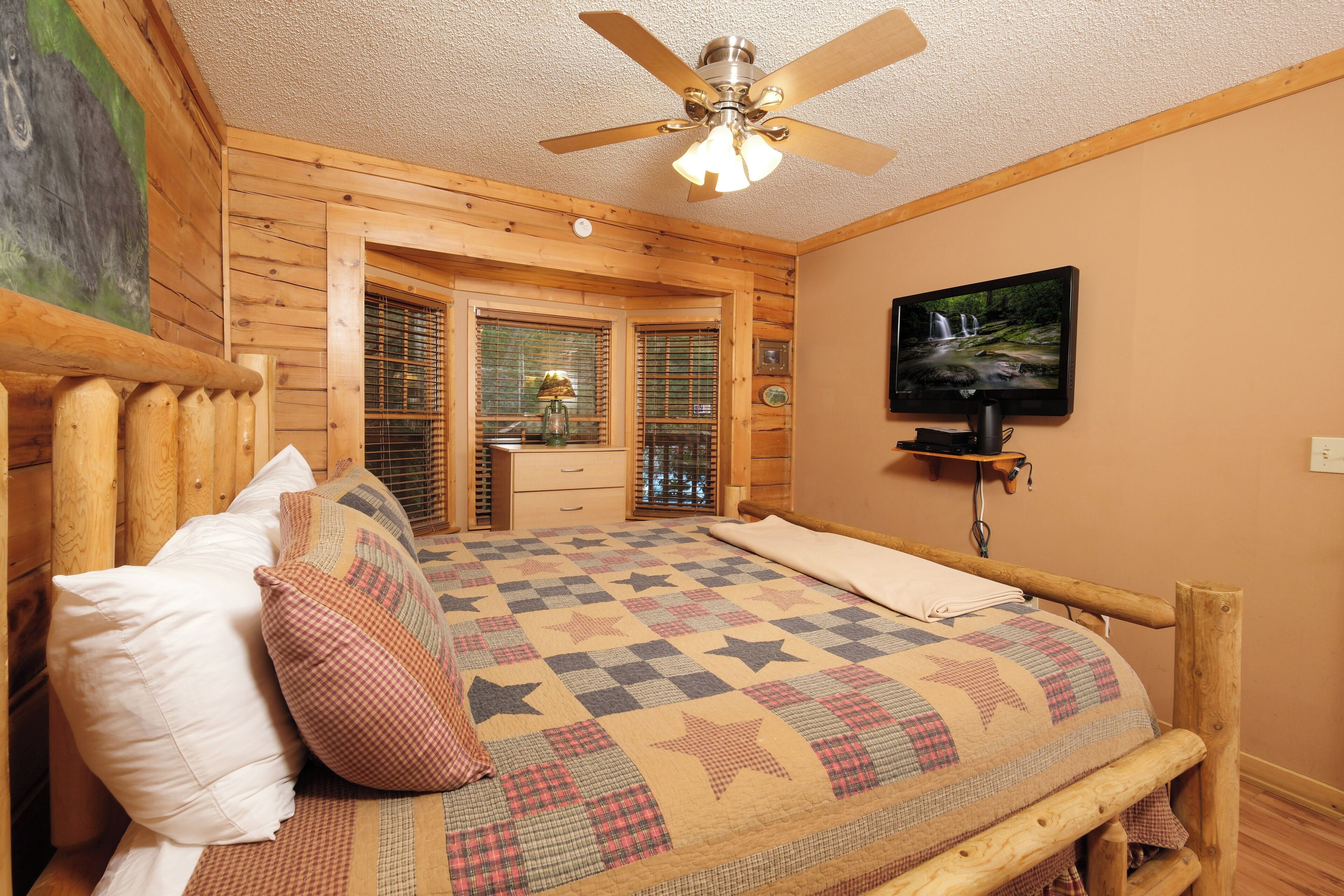 Un dormitorio de madera con una cama, un ventilador de techo, un televisor y una ventana con persianas.