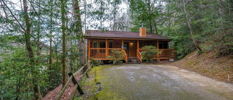 A cabin with a wooden deck, surrounded by dense forest.