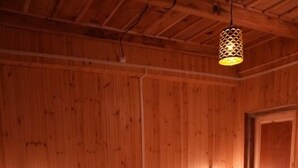 Quarto com painéis de madeira, uma cama, duas mesas de cabeceira e um lustre.