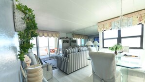 A modern living room with a striped sofa, a glass coffee table, and a chair. There is a large mirror reflecting the room and a balcony with a railing. - Beautiful 2BD/2 Bathroom direct ocean front located closer to downtown . (OCEAN CITY)