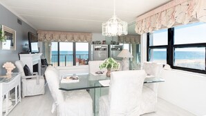 A modern living room with a glass dining table, white upholstered chairs, a chandelier, and a view of the sea through large windows. - Beautiful 2BD/2 Bathroom direct ocean front located closer to downtown . (OCEAN CITY)