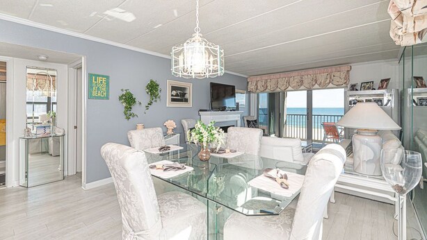 A dining area with a glass table, white upholstered chairs, a chandelier, and a view of the beach through large windows. - Beautiful 2BD/2 Bathroom direct ocean front located closer to downtown . (OCEAN CITY)