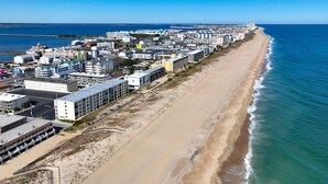 A coastal cityscape with a long beachfront, buildings, and a clear sky. - Beautiful 2BD/2 Bathroom direct ocean front located closer to downtown . (OCEAN CITY)