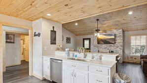A modern kitchen with white cabinetry, a built-in dishwasher, and a stone backsplash. - Cozy 3 Bedroom with King Beds, Mountain View, Game Room, WiFi, Hot Tub, Fire Pit (Sevierville)