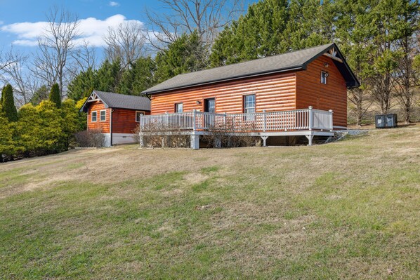A wooden cabin with a balcony, surrounded by trees and a grassy area.