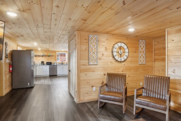 A wooden interior with a kitchen, two chairs, a clock, and a refrigerator. - 2 Bedroom with Fire Pit, Mountain View, WiFi and Private Game Room! (Sevierville)