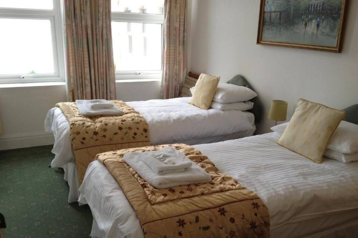 Two twin beds with floral-patterned bedspreads and white linens, a painting on the wall, and a window with curtains.