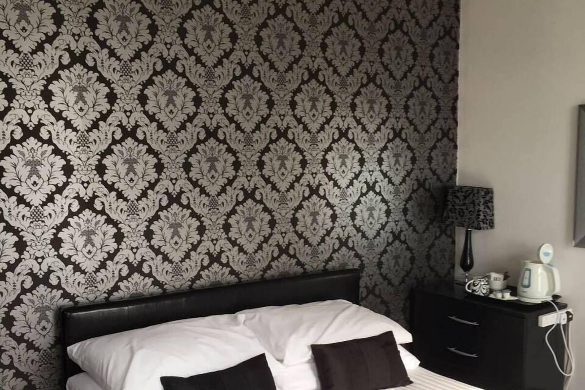 A neatly made bed with white and black bedding, a black headboard, and a patterned wallpaper.