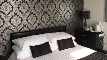 A neatly made bed with white and black bedding, a black headboard, and a patterned wallpaper.