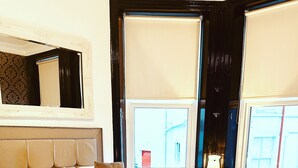 Un dormitorio bien equipado con una cama grande, una mesita de noche, una lámpara y una ventana con persianas.