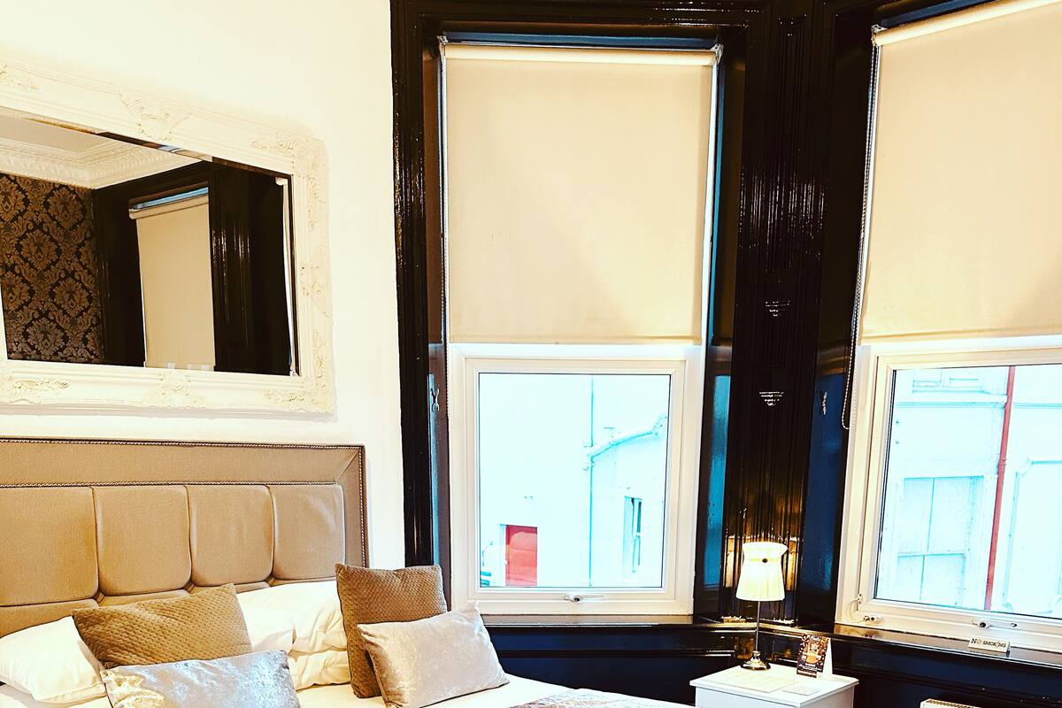 A well-appointed bedroom with a large bed, a nightstand, a lamp, and a window with blinds.