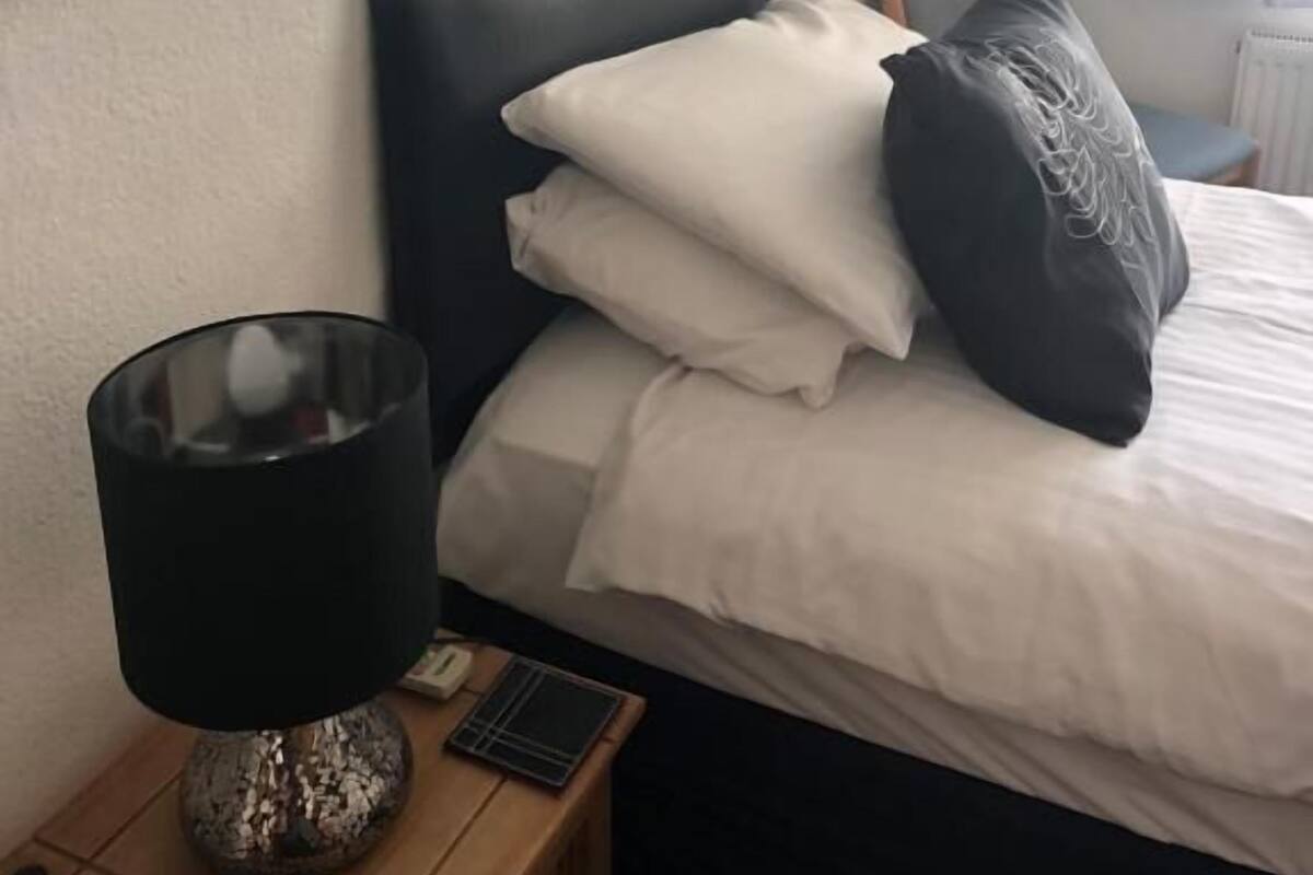 A hotel room with a bed, a bedside table with a lamp, and a large mirror on the wall.