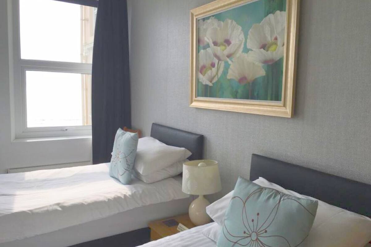 A hotel room with two beds, a painting of flowers on the wall, and a window with curtains.