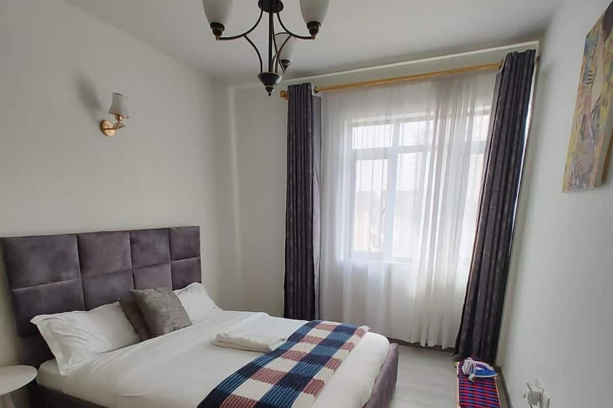 Un dormitorio con una cama grande, una araña, una ventana con cortinas y una pequeña mesa con una silla.