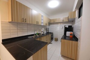 A modern kitchen with wooden cabinets, a black countertop, and white tiled walls. - Lux Suites Sandalwood  Apartments (Nairobi)