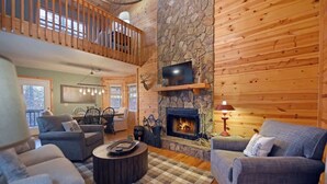 A cozy cabin interior with a stone fireplace, wooden walls, a balcony, and a dining area. - Hayden’s Hideaway - View, hot tub, game room, fun! (Blairsville)
