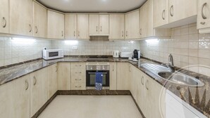 A kitchen with beige cabinets, a microwave, a stove, and a sink. - La Manga Club Bellaluz Apartment 603 (Atamaría)