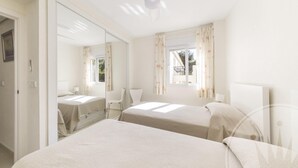 A bedroom with two beds, a ceiling fan, a window with curtains, and a mirror reflecting the room. - La Manga Club Bellaluz Apartment 603 (Atamaría)