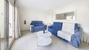A living room with two blue sofas, a white coffee table, and a large window with curtains. - La Manga Club Bellaluz Apartment 603 (Atamaría)